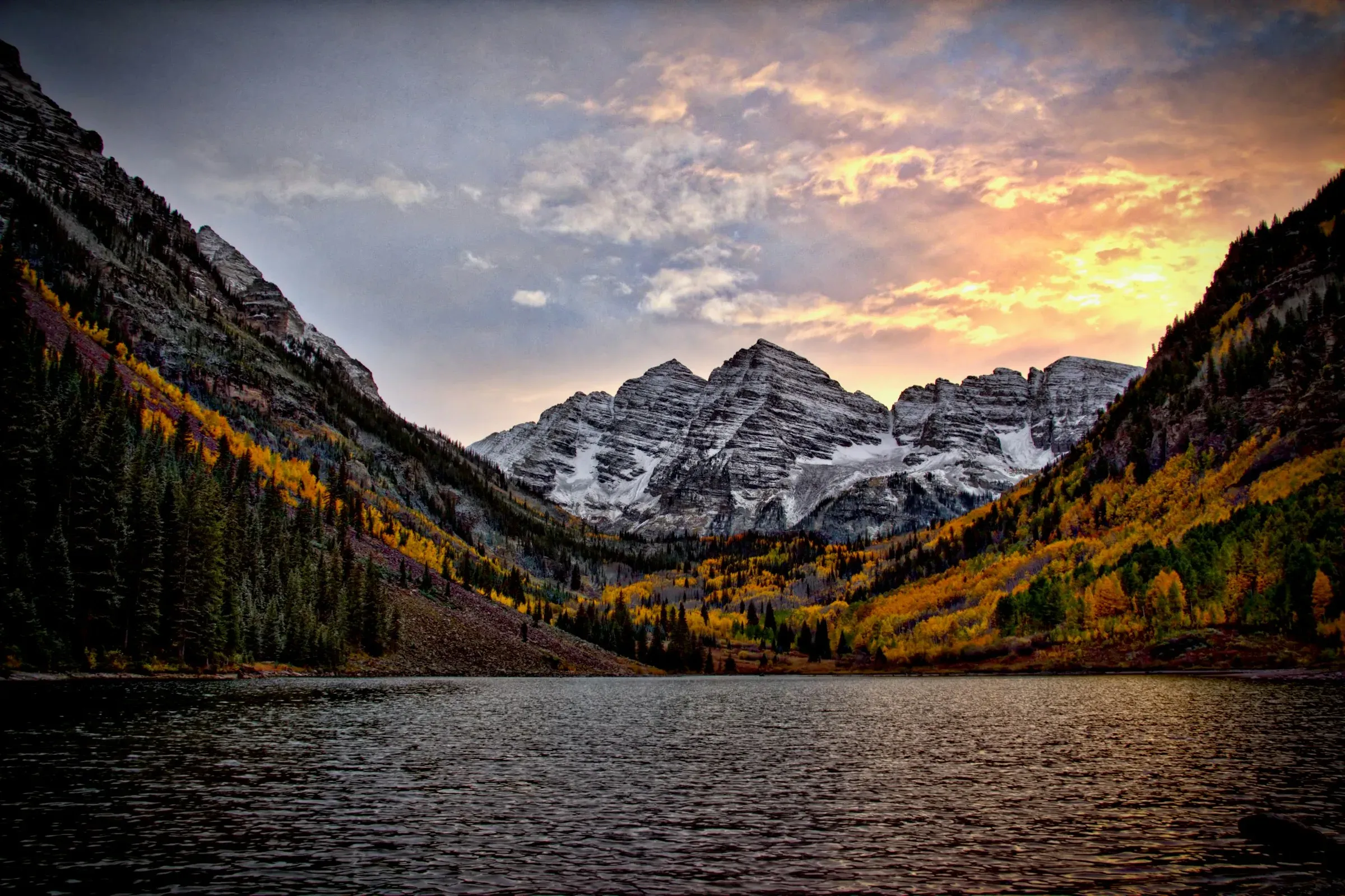 The Maroon Bells in Colorado at sunset, snow-streaked peaks above golden aspens and Maroon Lake.